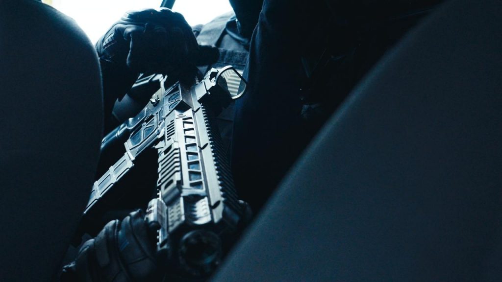 Nahaufnahme eines SWAT-Agenten im Auto, der eine Waffe nachlädt. Er trägt schwarze Handschuhe und eine schusssichere Weste.