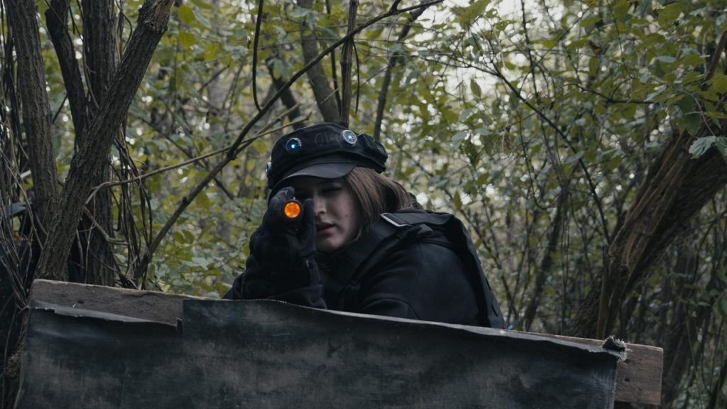 Eine SWAT-Agentin steht im Wald der Outdoor-Lasertag-Arena in Wels, schaut über eine Palette und zielt mit einer Pistole direkt in die Kamera. Szene aus dem Projekt "The Extraction" von XENTRA FILMS, gegründet von Jannis Danner.