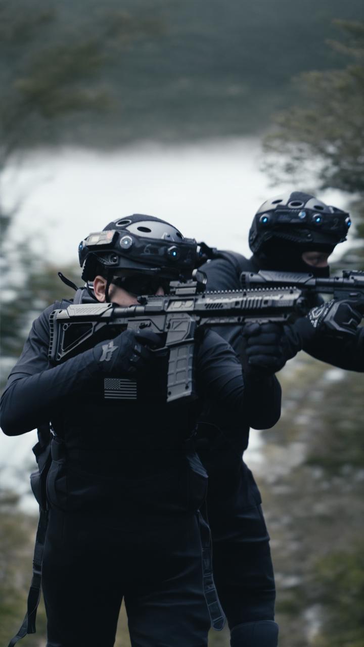 Zwei Männer in SWAT-Uniform mit Helm, Sturmhaube und Sonnenbrille halten jeweils eine Waffe, sie stehen im Wald bei der Outdoor-Lasertag-Arena von Lasertag Pro in Wels.