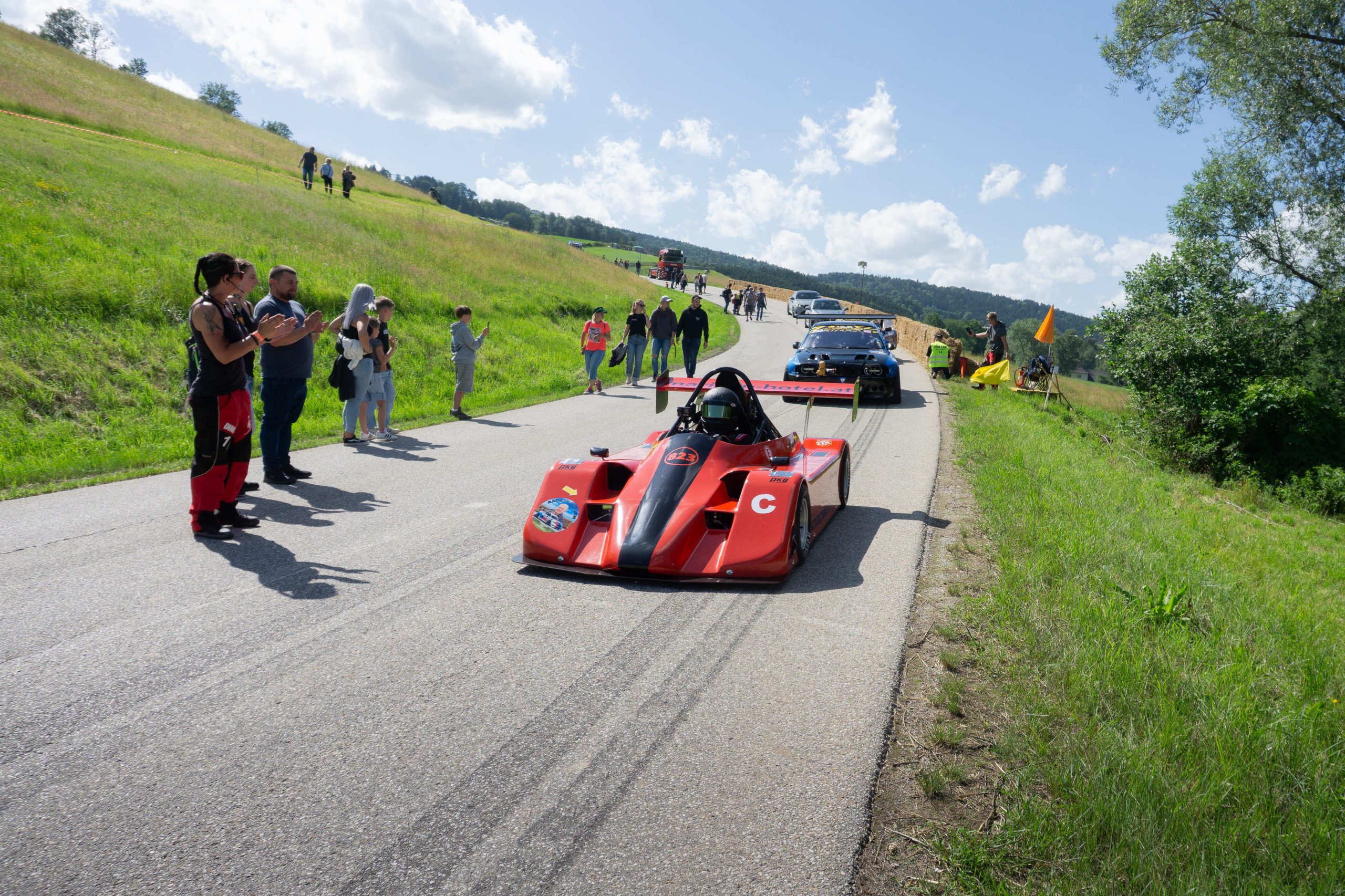 Roter Rennwagen bei der Rückführung auf der Strecke des Julbach Bergrennens, daneben Streckenposten