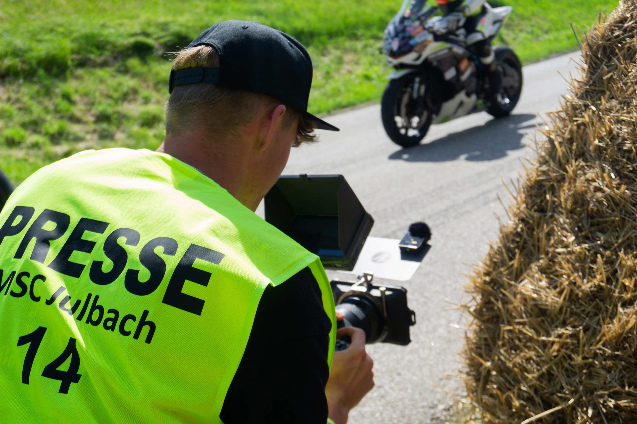 Jannis Danner in Presseweste filmt einen Motorradfahrer an den Strohballen beim Bergrennen Julbach