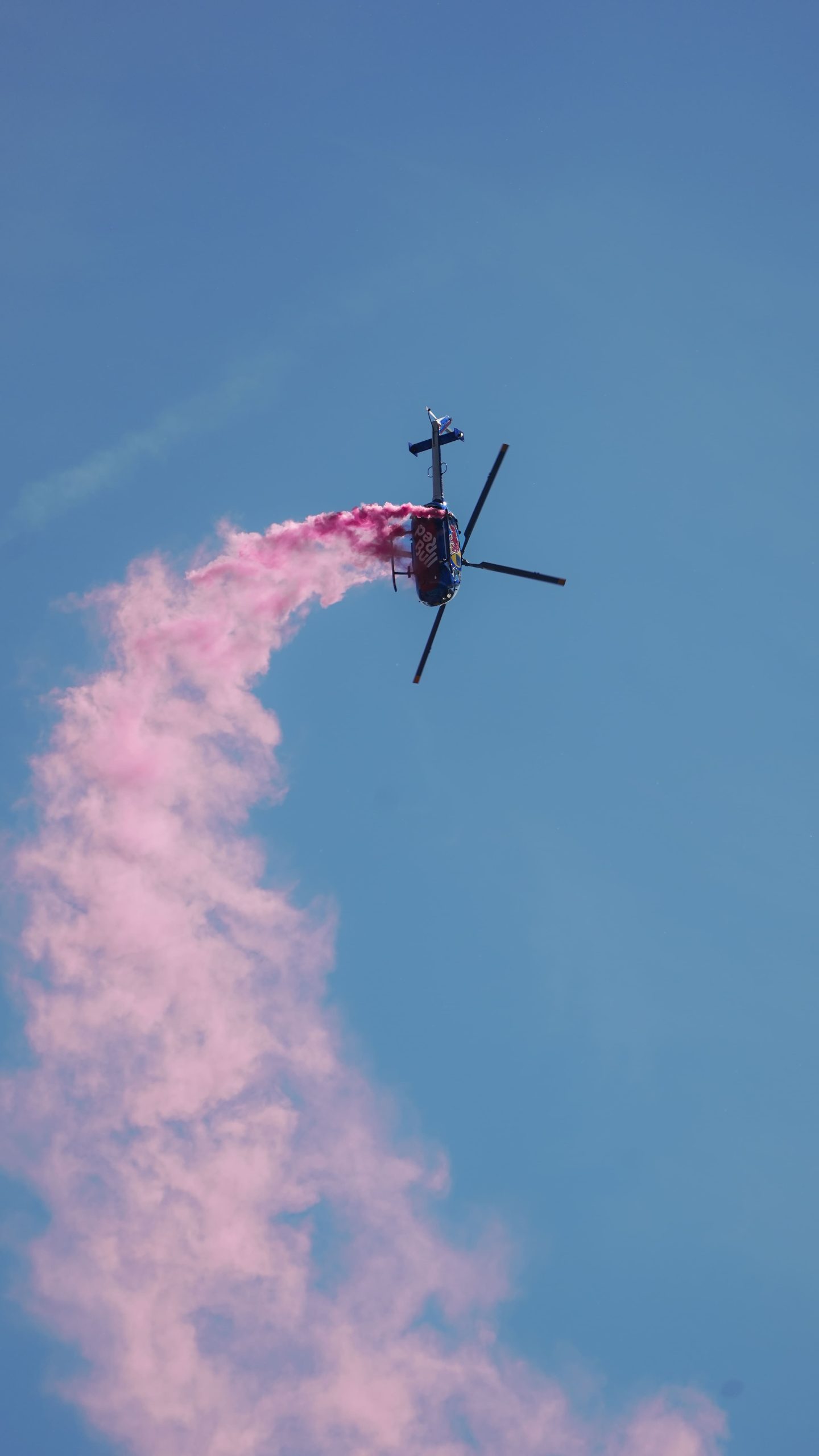 Hubschrauber BO 105 C der Flying Bulls im Kunstflug mit pinkem Rauch am blauen Himmel
