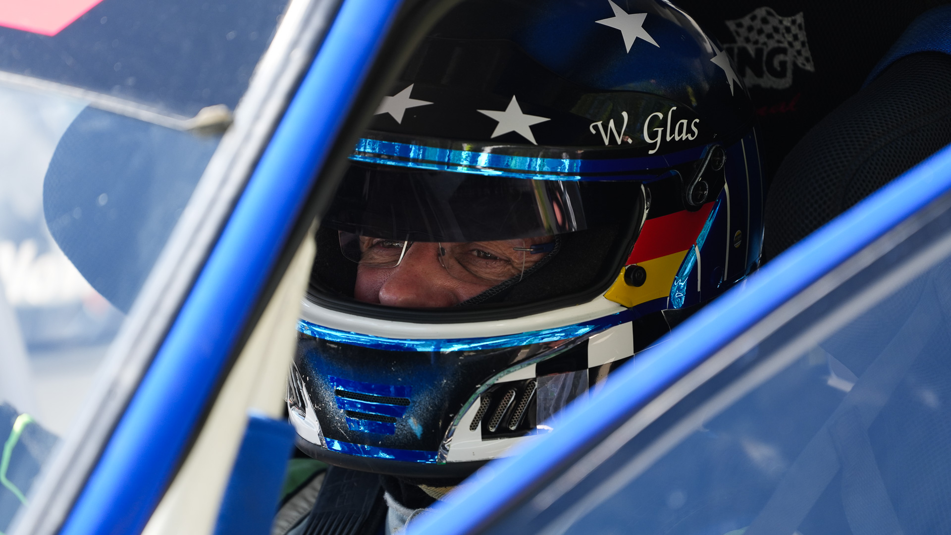 Fahrer W. Glas mit blau weißem Helm sitzt konzentriert im Cockpit seines Fahrzeugs