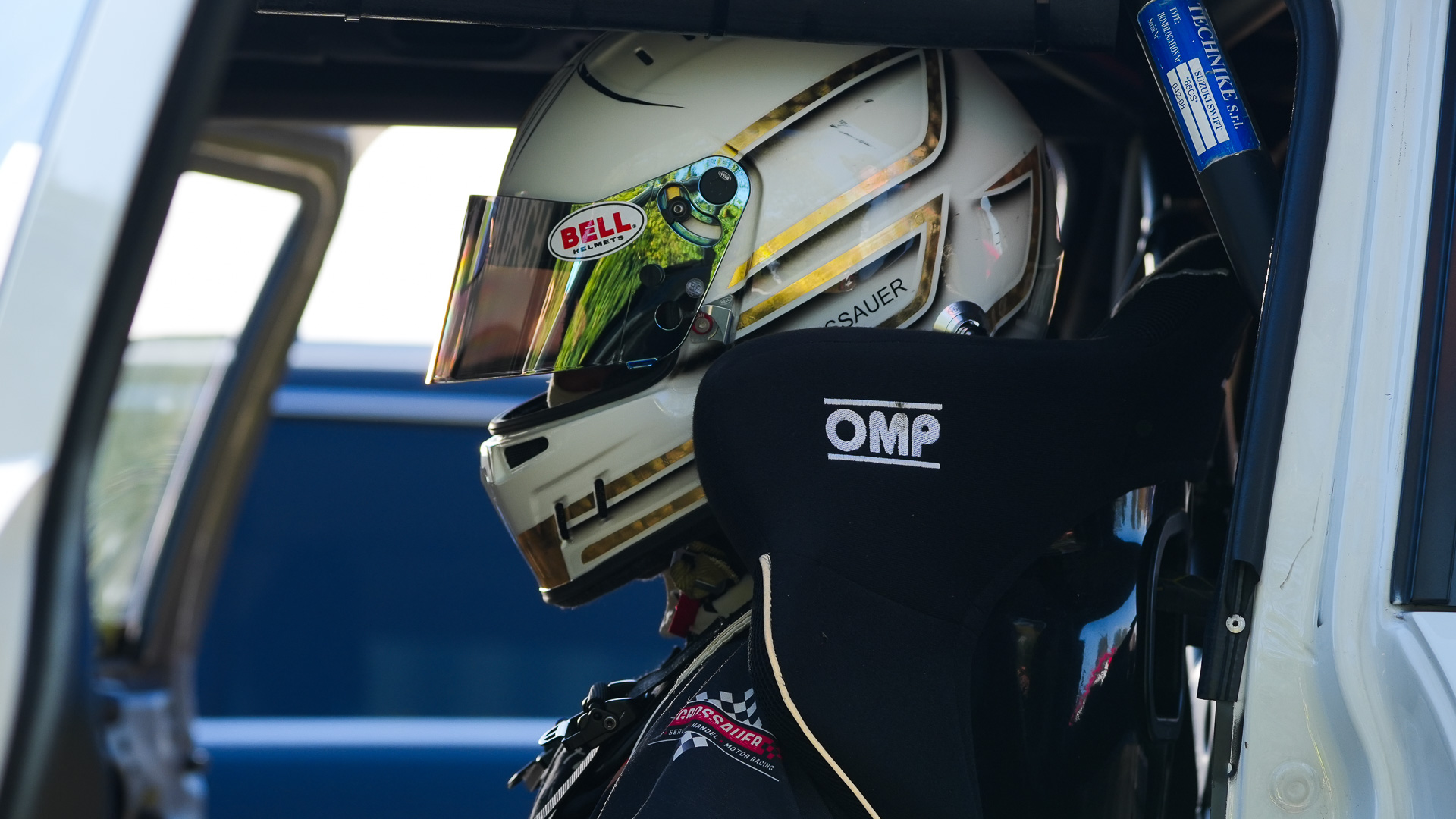 Fahrer mit grün weißem OMP Helm sitzt im Cockpit des blauen Rennfahrzeugs