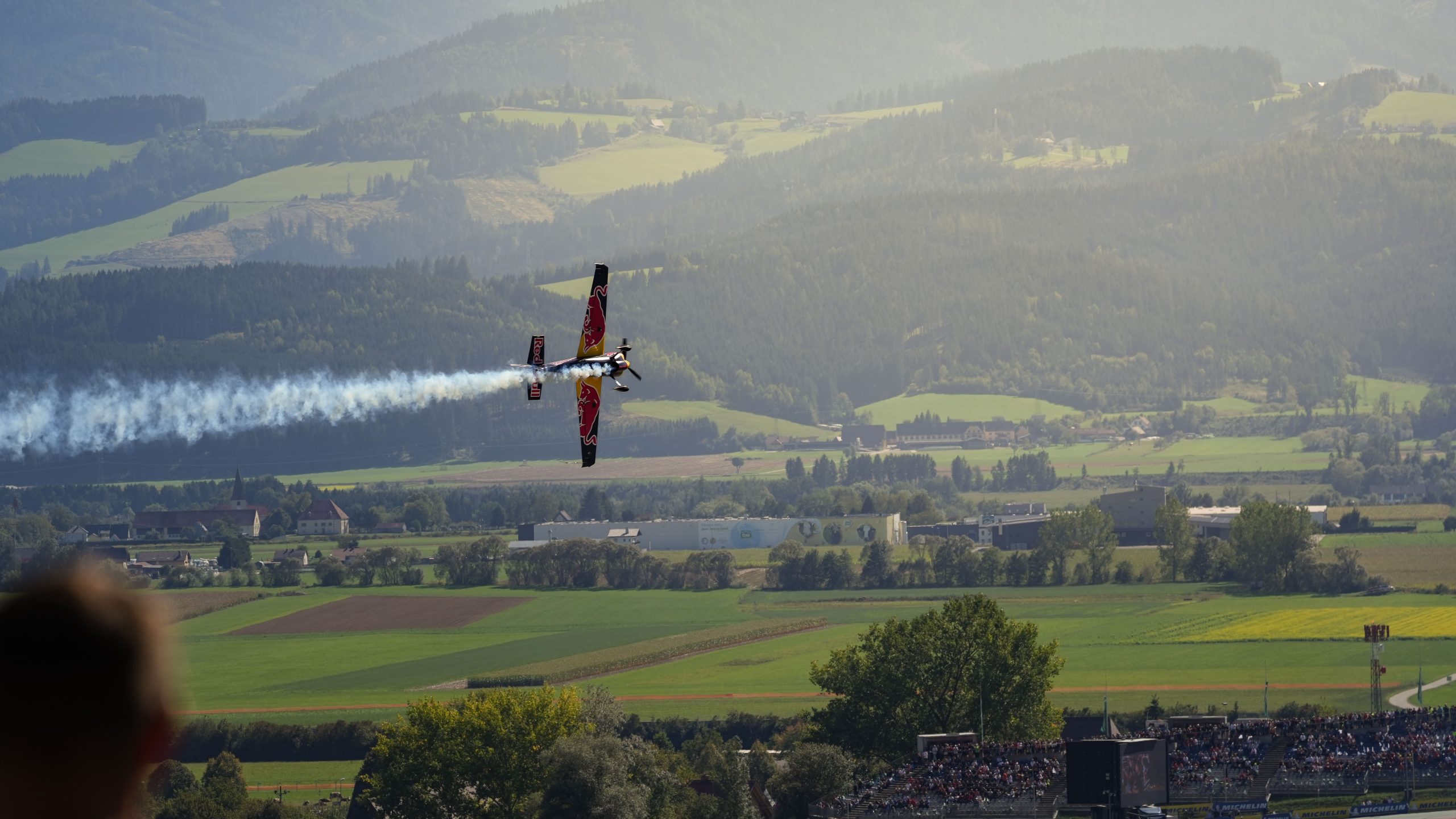 Kunstflugzeug der Flying Bulls mit Rauchspur vor den grünen Hügeln des Murtals
