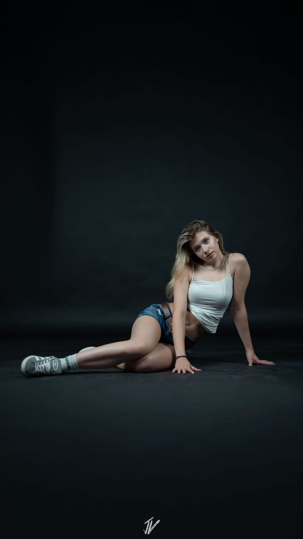 Model Naemi Krösche sitzend auf dem Boden vor schwarzem Hintergrund im Studio