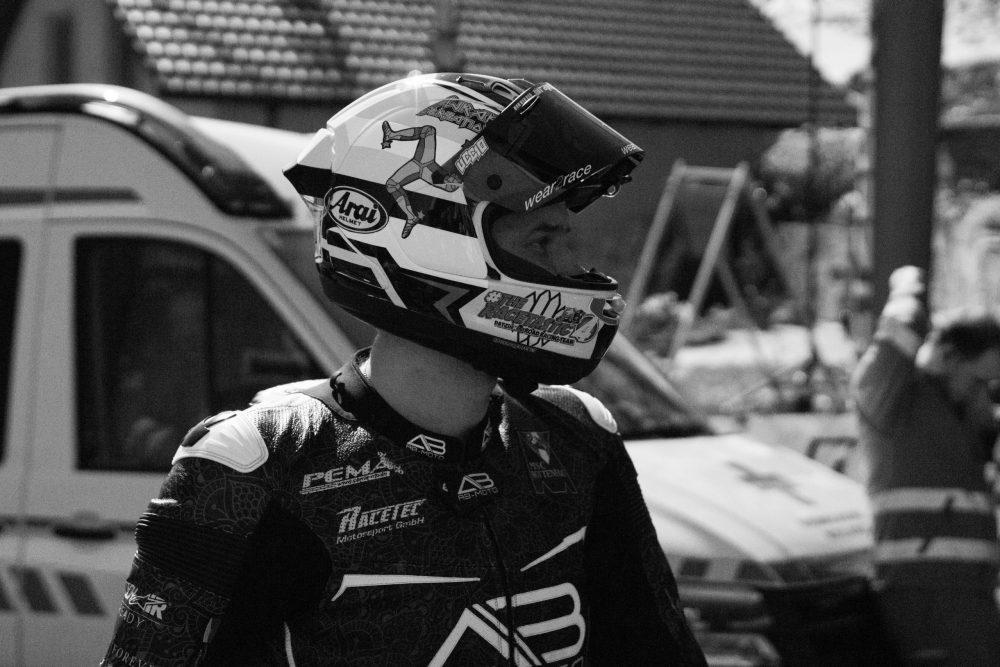 Landshaag Bergrennen 2026 | Oberösterreich Thomas Altendorfer in Lederkombi mit weißem Helm im Fahrerlager beim Landshaag Bergrennen 2026, Schwarzweißfoto