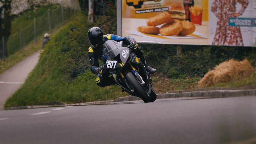 Landshaag Bergrennen 2026 | Oberösterreich Motorradfahrer in Schräglage in Kurve 1 beim Landshaag Bergrennen 2026, dahinter eine Plakatwand