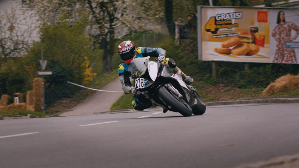 Landshaag Bergrennen 2026 | Oberösterreich Motorradfahrer auf Superbike in Weiß und Blau in Kurve 1 vor Plakatwand beim Landshaag Bergrennen 2026