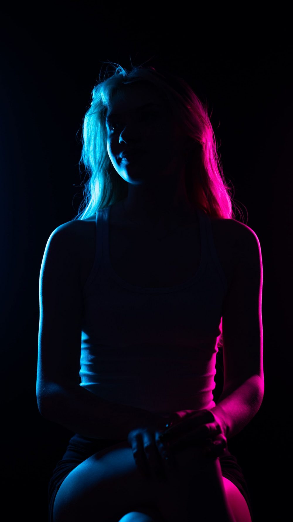 Naemi Krösche Model Shooting | HTL Paul Hahn, Linz Naemi Krösche sitzt im Gegenlicht in blauem und pinkem Licht mit gesenktem Blick