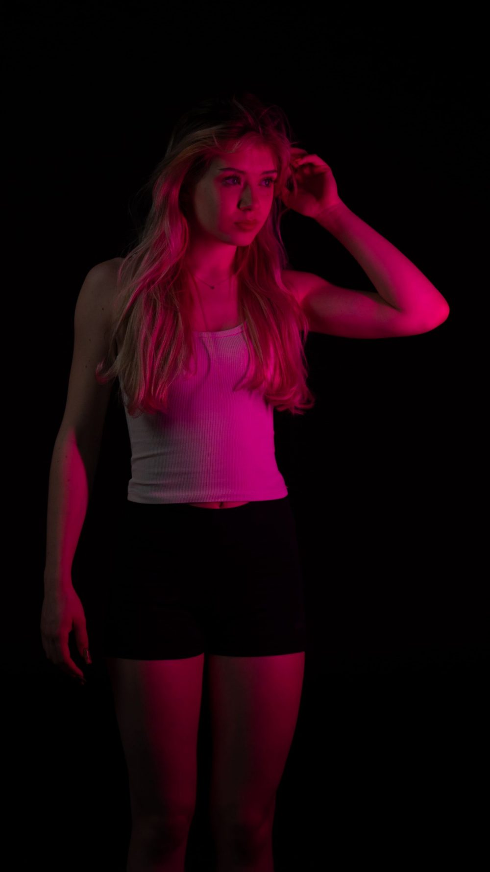 Naemi Krösche Model Shooting | HTL Paul Hahn, Linz Naemi Krösche steht mit einer Hand im Haar in pinkem Licht vor dunklem Hintergrund