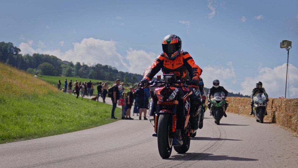 Bergrennen Julbach 2026 | Julbach, Oberösterreich Fahrer in oranger Lederkombi führt die Gruppe bei der Rückführung an den Zuschauern vorbei in Julbach
