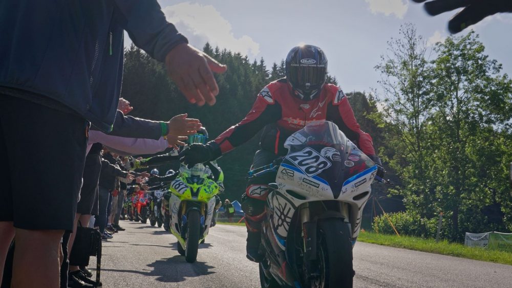 Bergrennen Julbach 2026 | Julbach, Oberösterreich Fahrer in roter Lederkombi klatscht bei der Rückführung einen Zuschauer ab, Bergrennen Julbach 2026