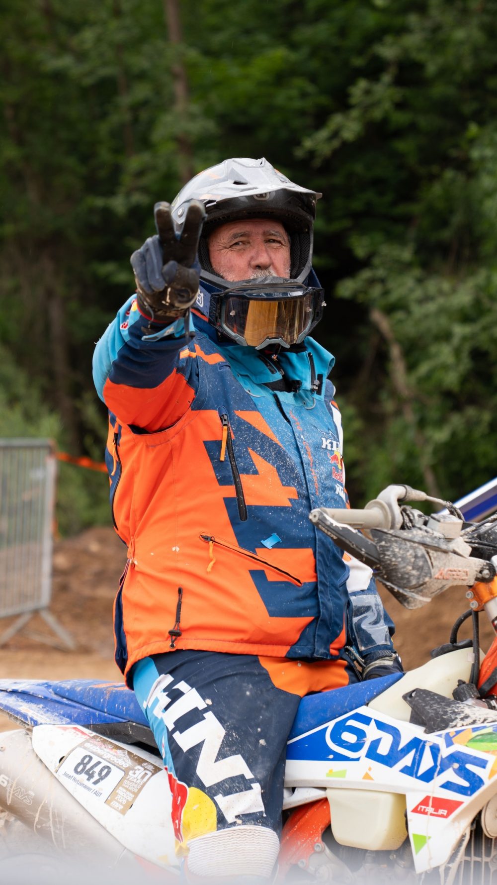 Endurofahrer grüßt vor dem Start in die Kamera, seine Ausrüstung in Orange und Blau