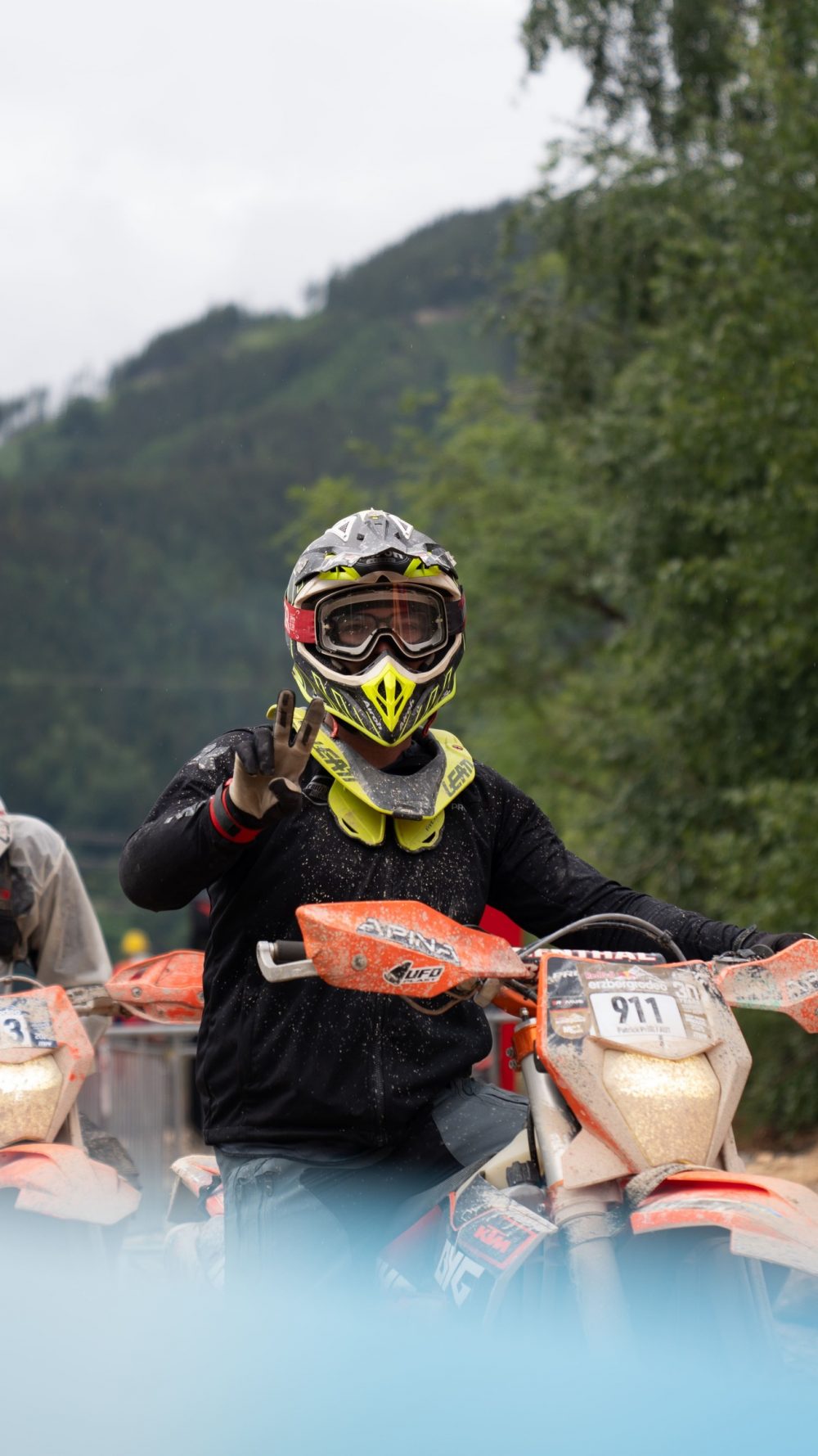 Endurofahrer mit neongelbem Helm zeigt im Startbereich in die Kamera