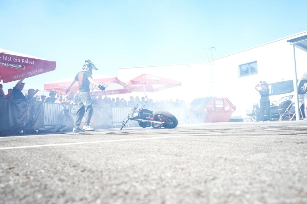 Stuntshow im Reifenrauch vor Zuschauern unter roten Schirmen beim AB Moto Sommerfest 2026