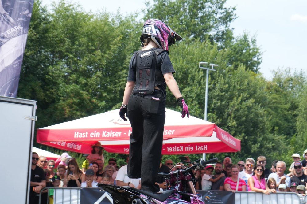 Stuntfahrerin mit pinkem Helm steht vor dem Publikum auf ihrem Motorrad