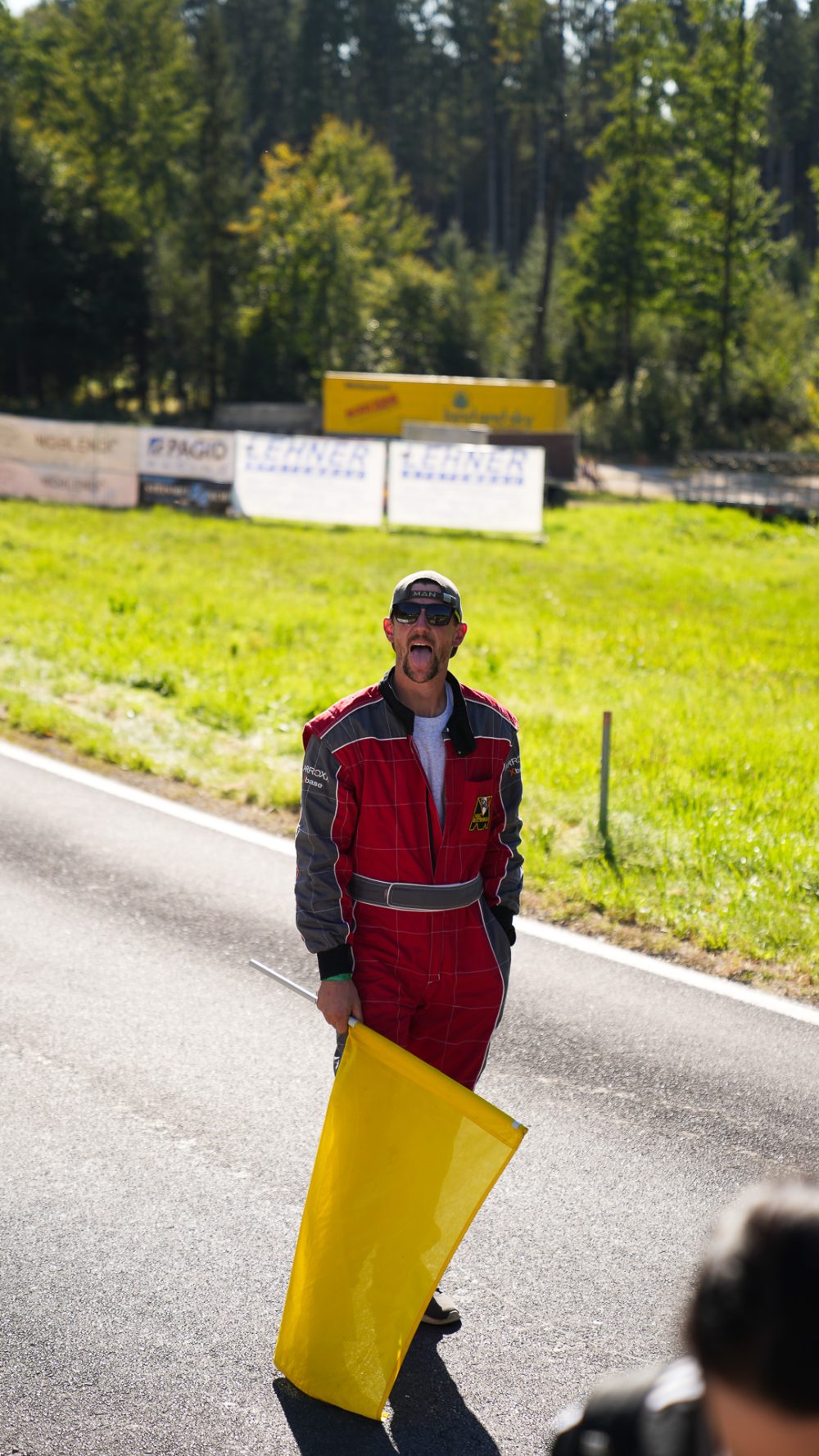 Bergrennen St. Agatha 2026 | Oberösterreich Streckenposten in rotem Overall steht mit gelber Flagge auf der leeren Rennstrecke