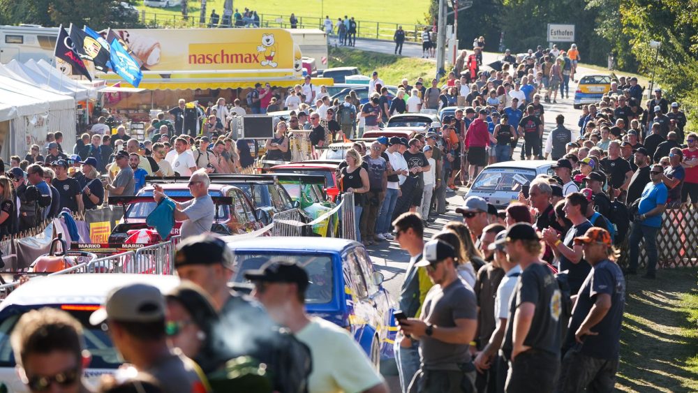 Warten auf den Start Rennwagen in langer Reihe zwischen Zuschauern im Fahrerlager, Zelte und Wiesen im Hintergrund