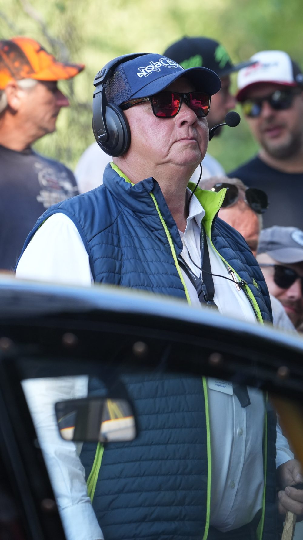 Rennorganisation im Einsatz Offizieller mit Headset, Sonnenbrille und blauer Weste steht neben einem Rennwagen