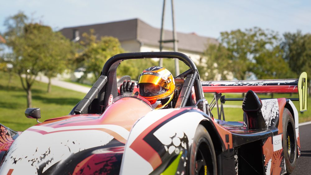 Sportprototyp in der Startaufstellung Offener Sportprototyp in Weiß, Orange und Schwarz mit Fahrer im gelben Helm