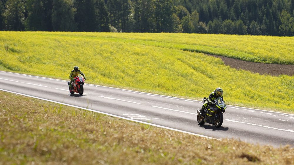 Motorräder an der Strecke Zwei Motorradfahrer auf einer Landstraße neben einem gelb blühenden Rapsfeld