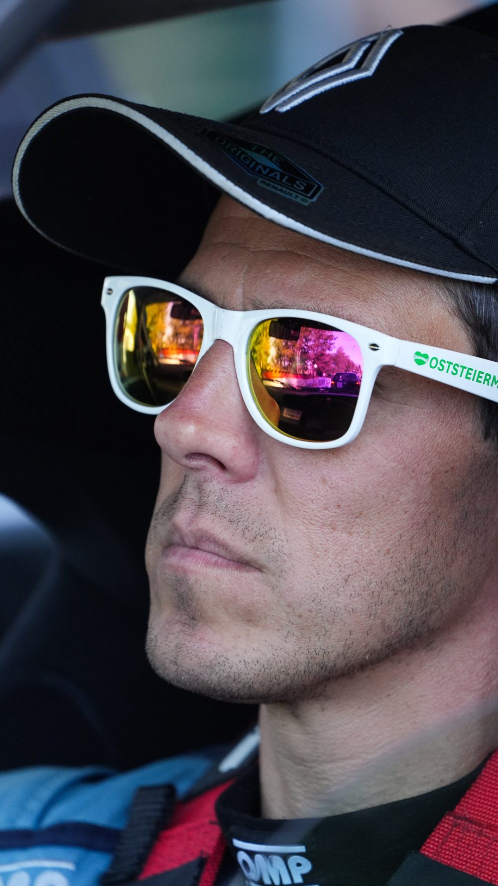 Konzentrierter Blick Fahrer mit schwarzer Kappe und weißer verspiegelter Sonnenbrille im roten Overall blickt konzentriert zur Seite