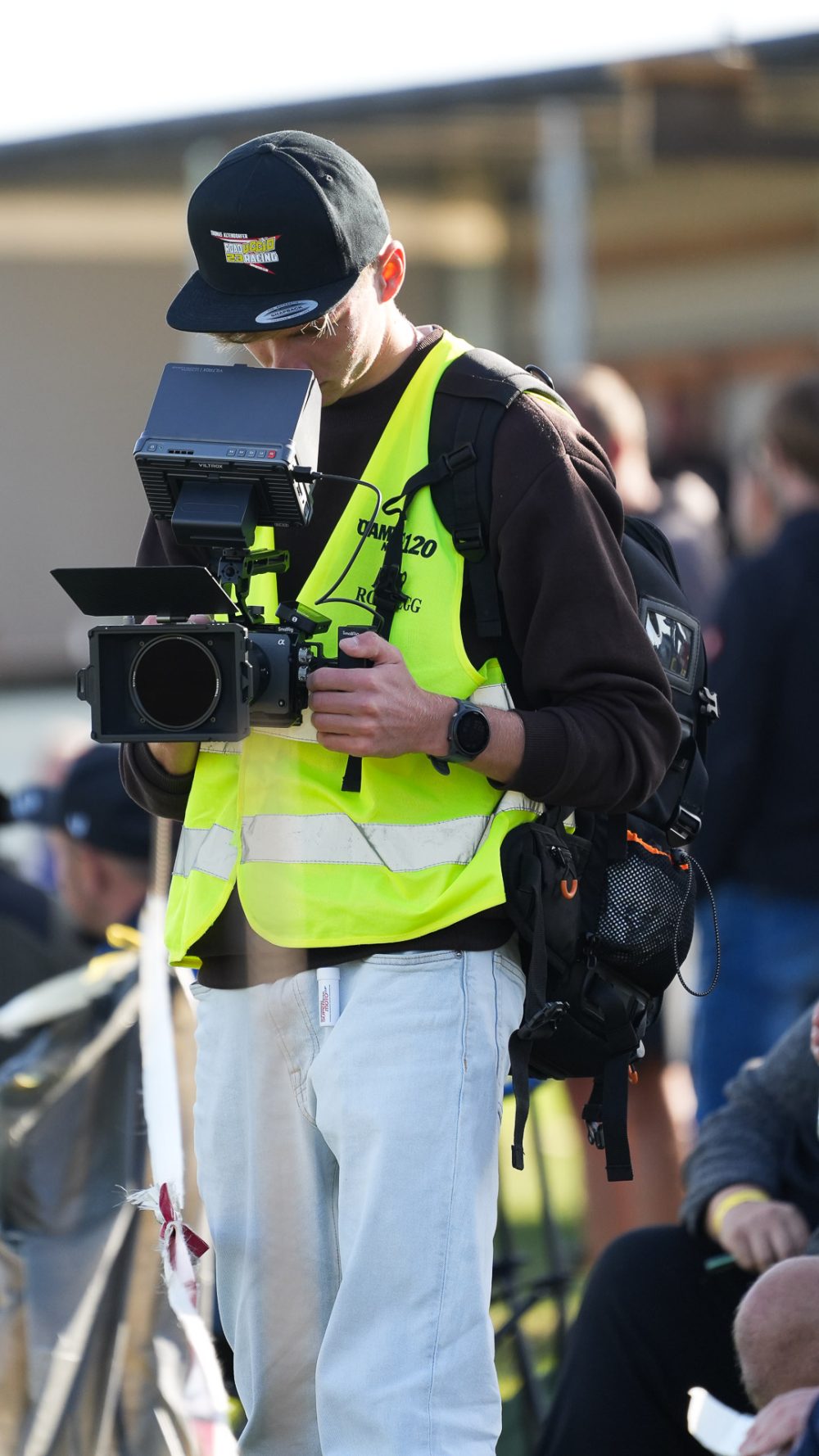 Videograf bei der Arbeit Kameramann in neongelber Warnweste hält eine Videokamera am Streckenrand