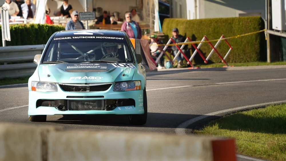 Lancer Evolution Türkisfarbener Mitsubishi Lancer Evolution frontal in der Kurve, Zuschauer und Absperrband im Hintergrund