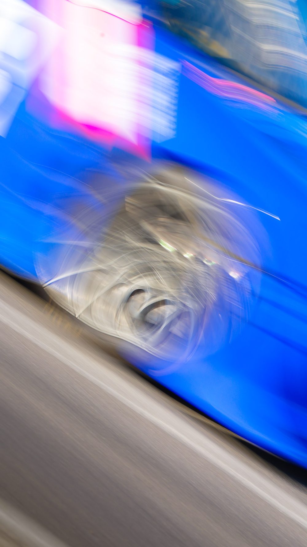 Bewegung im Bild Abstrakte Mitzieher-Aufnahme eines blauen Rennwagens mit verwischtem Rad