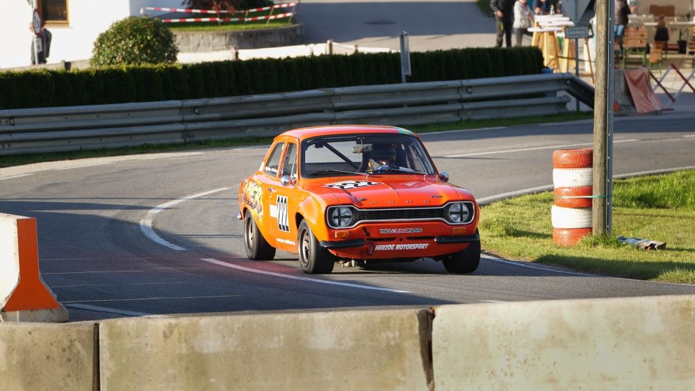Ford Escort in der Kurve Orangefarbener Ford Escort Rennwagen in der Kurve vor Hecke und Leitplanke