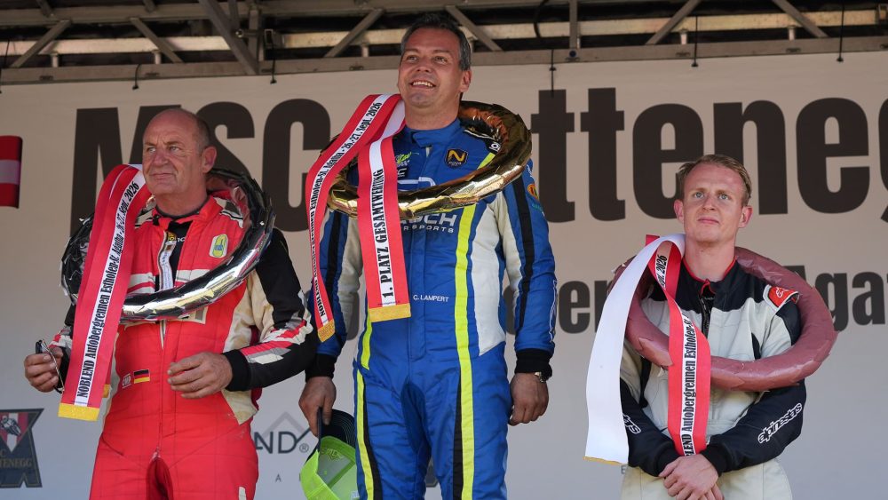 Die Sieger auf dem Podium Drei Fahrer in Rot, Blau und Weiß mit Siegerkränzen lächeln vor dem Banner des MSC Rottenegg